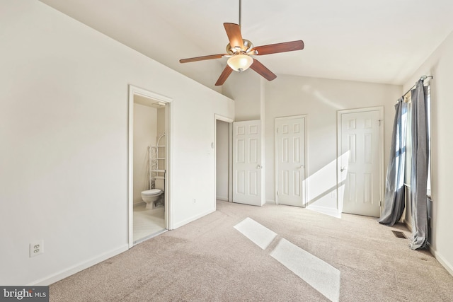 unfurnished bedroom featuring lofted ceiling, ceiling fan, ensuite bathroom, light colored carpet, and multiple closets