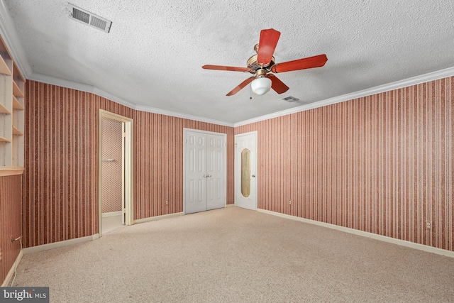 carpeted spare room featuring ceiling fan, ornamental molding, and a textured ceiling