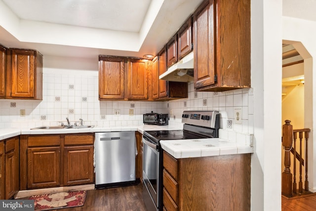 kitchen featuring appliances with stainless steel finishes, backsplash, a raised ceiling, dark wood-type flooring, and sink