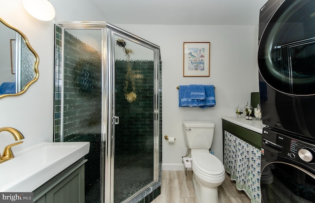 bathroom featuring vanity, toilet, a shower with shower door, and stacked washer and clothes dryer