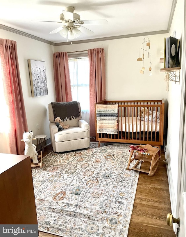 bedroom with ceiling fan, crown molding, a crib, and hardwood / wood-style flooring