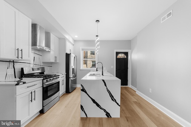 kitchen with white cabinetry, wall chimney exhaust hood, stainless steel appliances, pendant lighting, and light hardwood / wood-style floors