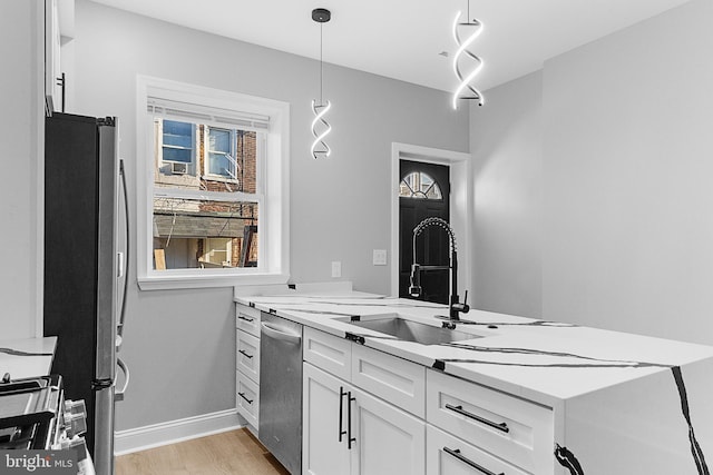 kitchen featuring white cabinets, sink, hanging light fixtures, light hardwood / wood-style flooring, and stainless steel appliances