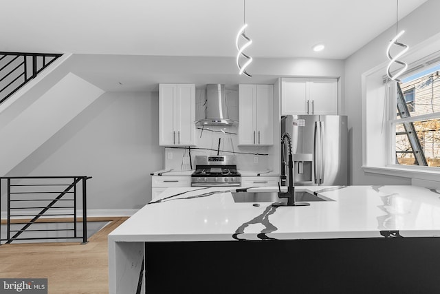 kitchen featuring pendant lighting, white cabinets, stainless steel appliances, and wall chimney range hood