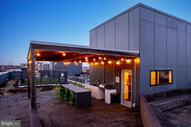 patio terrace at dusk featuring an outdoor kitchen and an outdoor wet bar