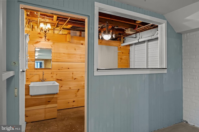 bathroom with wood walls, sink, concrete flooring, and brick wall