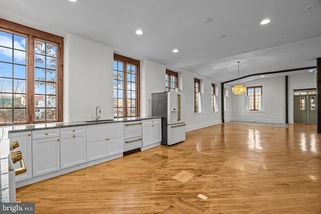 kitchen featuring stone counters, sink, refrigerator with ice dispenser, decorative light fixtures, and white cabinetry