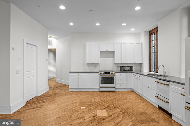 kitchen with white cabinetry, sink, stainless steel stove, and dark stone counters