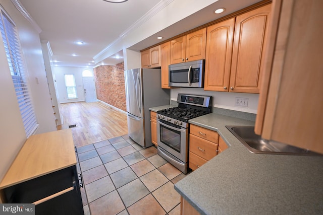 kitchen featuring light tile patterned flooring, appliances with stainless steel finishes, ornamental molding, and brick wall