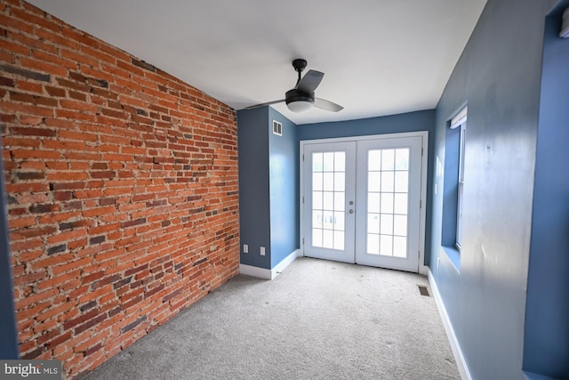 carpeted spare room with ceiling fan, french doors, and brick wall