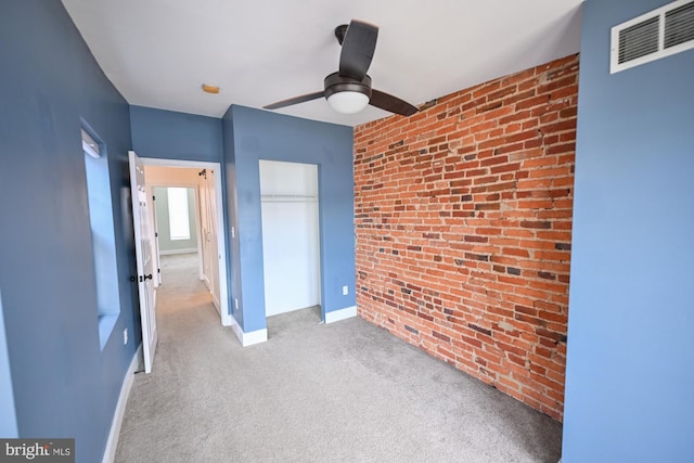 unfurnished bedroom with light carpet, a closet, ceiling fan, and brick wall