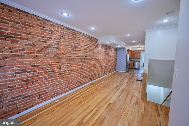 unfurnished living room with light hardwood / wood-style floors, crown molding, and brick wall