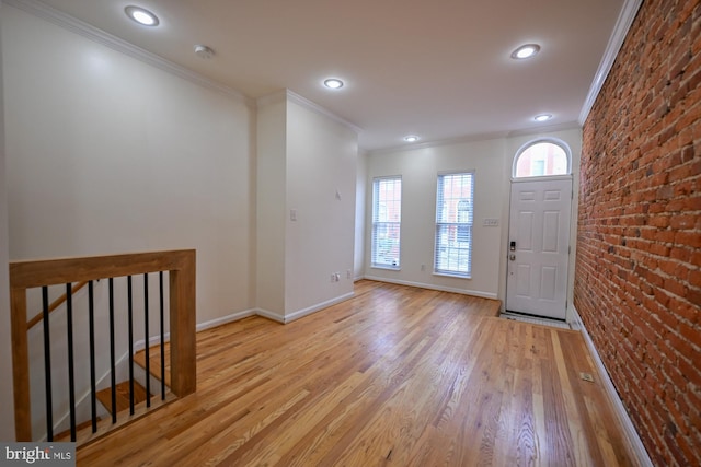 entrance foyer featuring crown molding, brick wall, and light hardwood / wood-style flooring