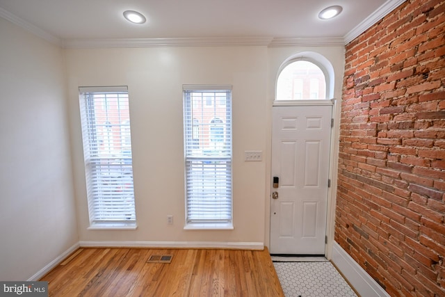 entrance foyer with light hardwood / wood-style flooring, a wealth of natural light, ornamental molding, and brick wall