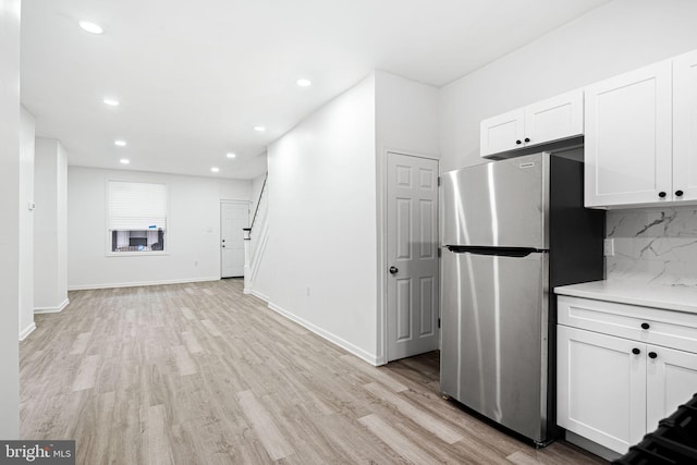 kitchen featuring white cabinets, decorative backsplash, stainless steel fridge, and light hardwood / wood-style floors