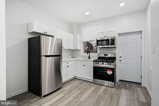 kitchen with white cabinets, light wood-type flooring, stainless steel appliances, and backsplash