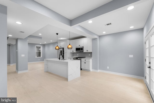 kitchen featuring sink, an island with sink, pendant lighting, light hardwood / wood-style floors, and white cabinets