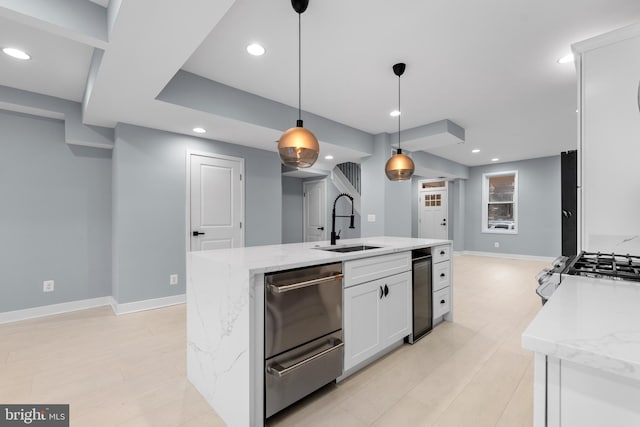 kitchen featuring white cabinetry, sink, light stone countertops, hanging light fixtures, and a kitchen island with sink