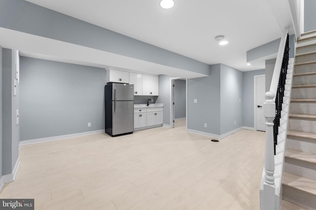 basement with stainless steel fridge, sink, and light wood-type flooring