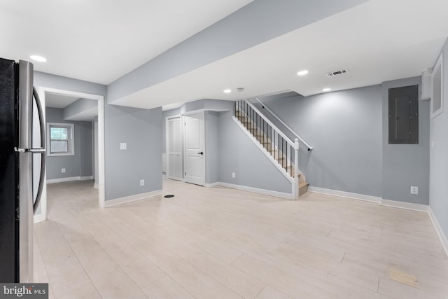 basement with stainless steel fridge, electric panel, and light hardwood / wood-style flooring