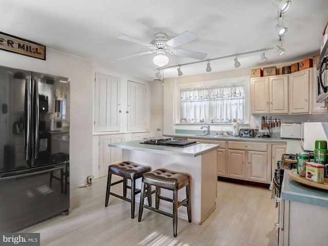 kitchen featuring ceiling fan, light hardwood / wood-style floors, appliances with stainless steel finishes, a kitchen island, and a kitchen bar