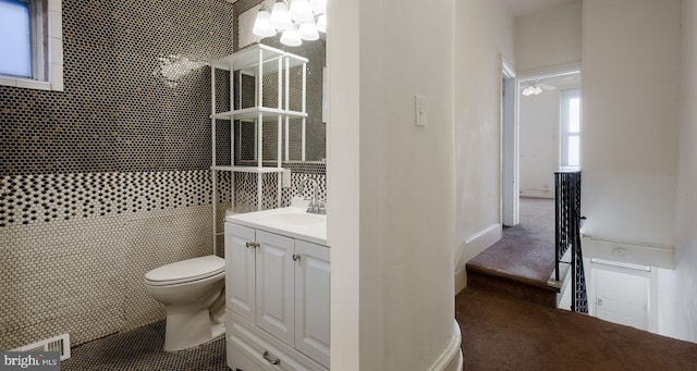 bathroom featuring a chandelier, vanity, toilet, and tile walls