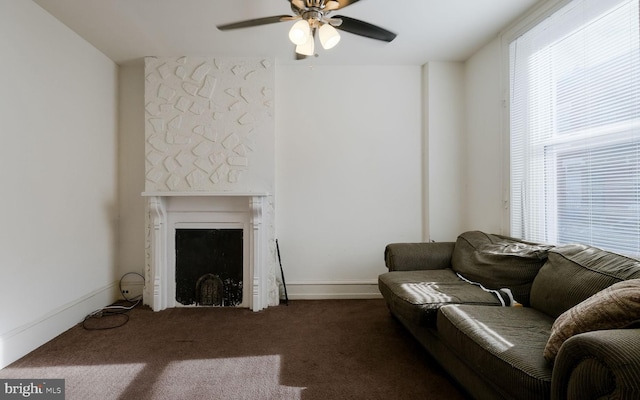 living room with ceiling fan, a large fireplace, and dark carpet