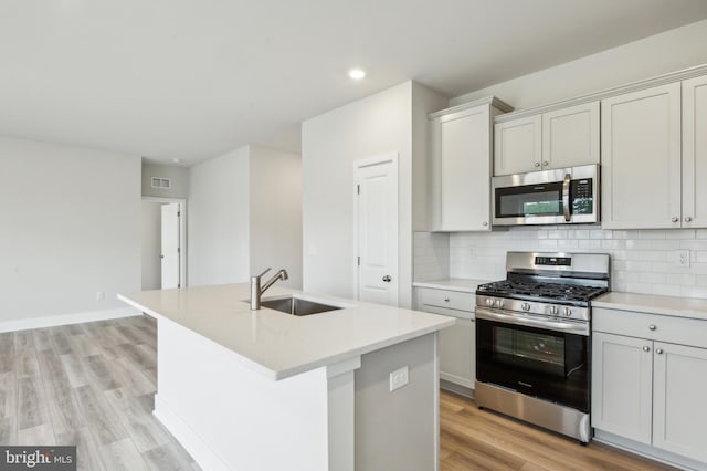 kitchen with sink, an island with sink, light hardwood / wood-style flooring, and appliances with stainless steel finishes