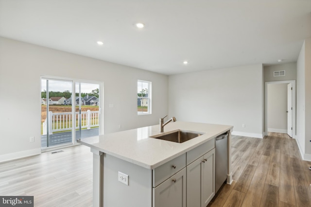 kitchen with light stone counters, sink, light hardwood / wood-style flooring, dishwasher, and an island with sink