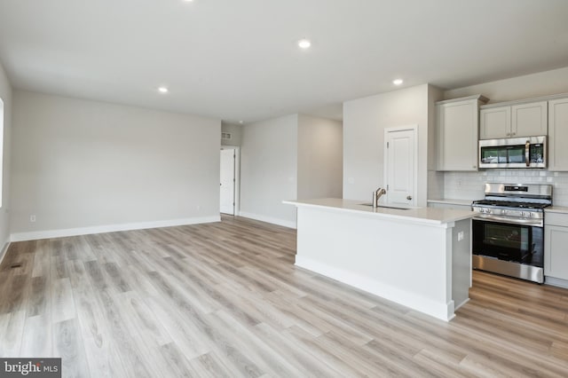 kitchen featuring a kitchen island with sink, sink, light wood-type flooring, appliances with stainless steel finishes, and tasteful backsplash