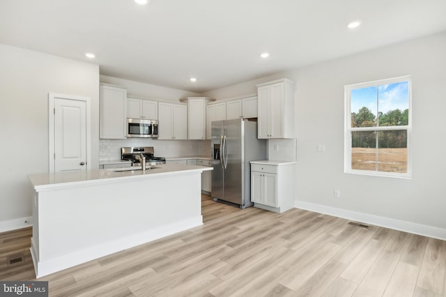 kitchen featuring appliances with stainless steel finishes, light hardwood / wood-style floors, white cabinetry, and an island with sink