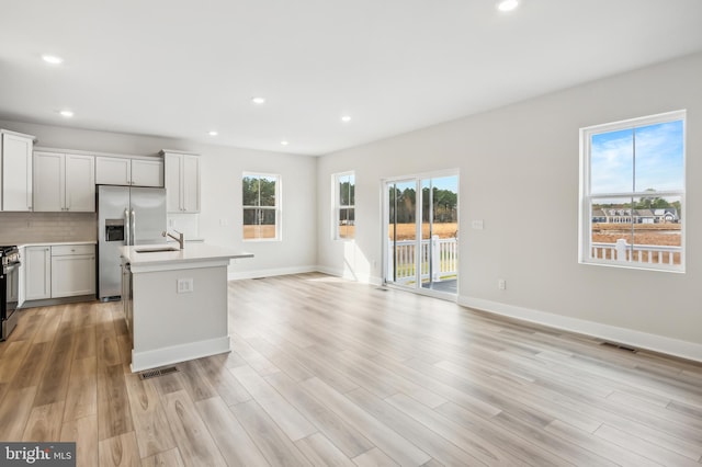 kitchen with a center island with sink, white cabinets, light wood-type flooring, and appliances with stainless steel finishes