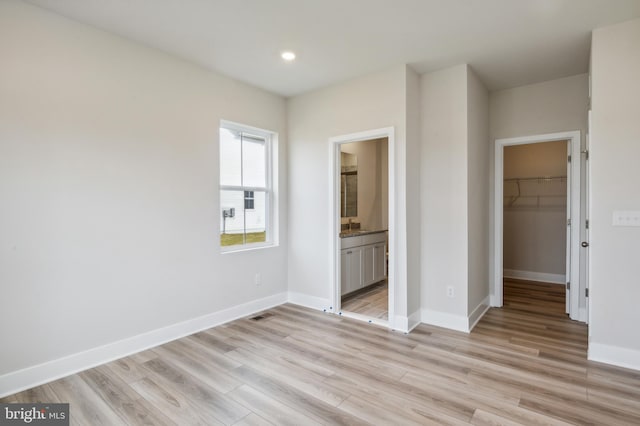 unfurnished bedroom featuring a walk in closet, ensuite bathroom, a closet, and light hardwood / wood-style floors