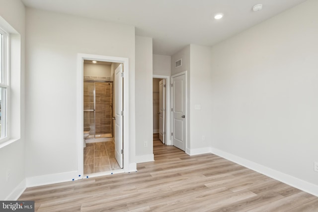 unfurnished bedroom featuring light wood-type flooring, ensuite bathroom, and multiple windows