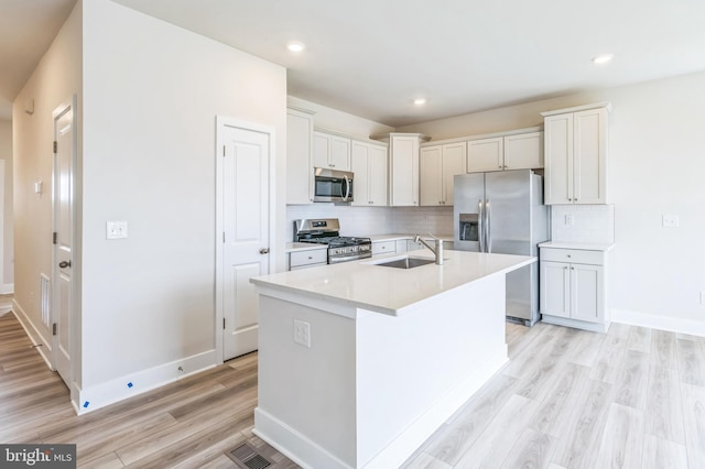 kitchen with stainless steel appliances, white cabinetry, a kitchen island with sink, and light hardwood / wood-style flooring