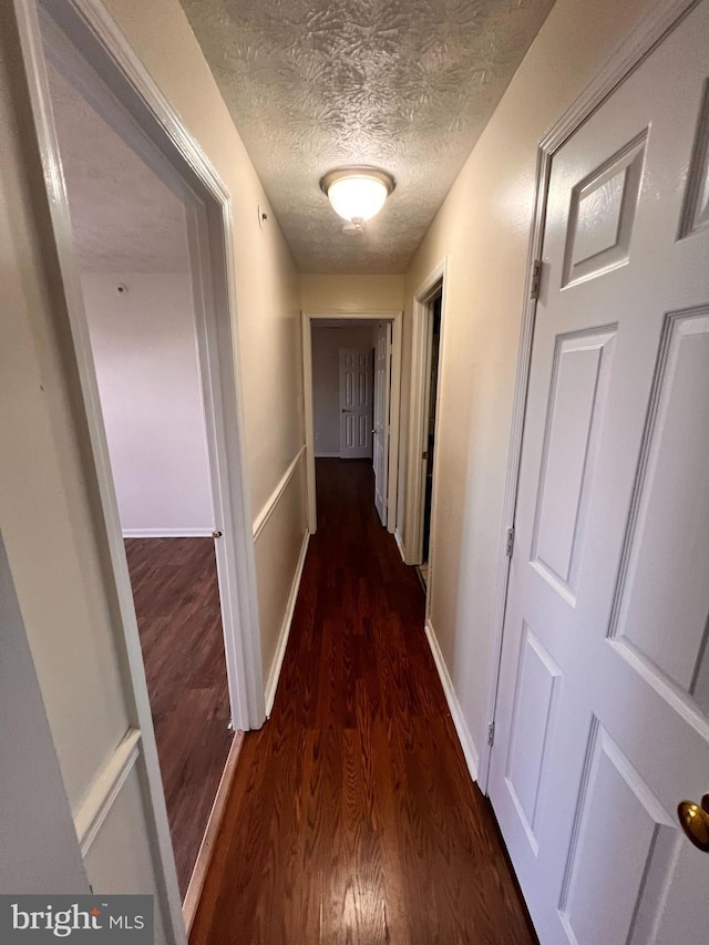 hall featuring a textured ceiling and dark wood-type flooring