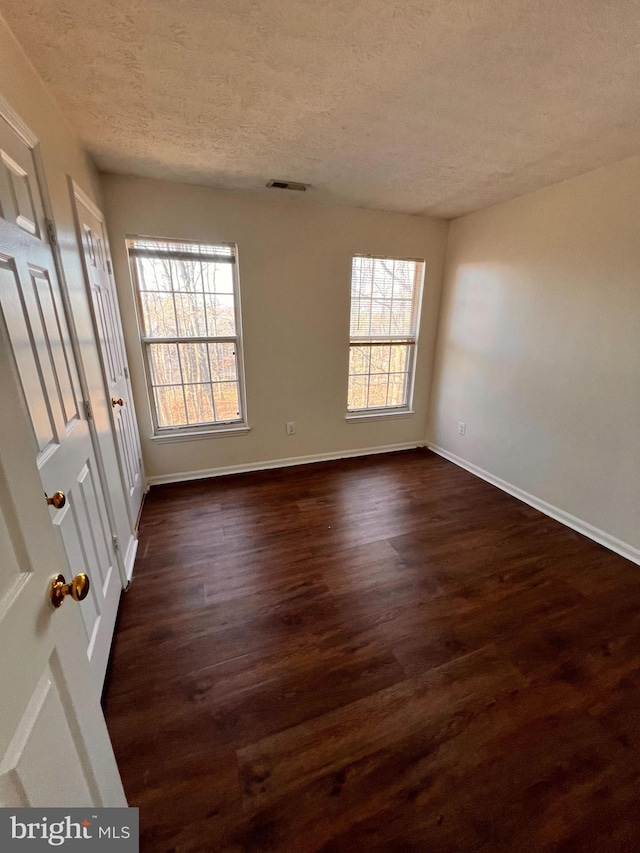 unfurnished room with a textured ceiling, plenty of natural light, and dark wood-type flooring