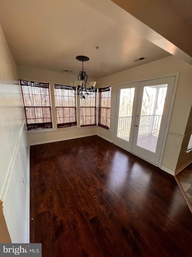 unfurnished dining area with french doors, an inviting chandelier, and dark wood-type flooring