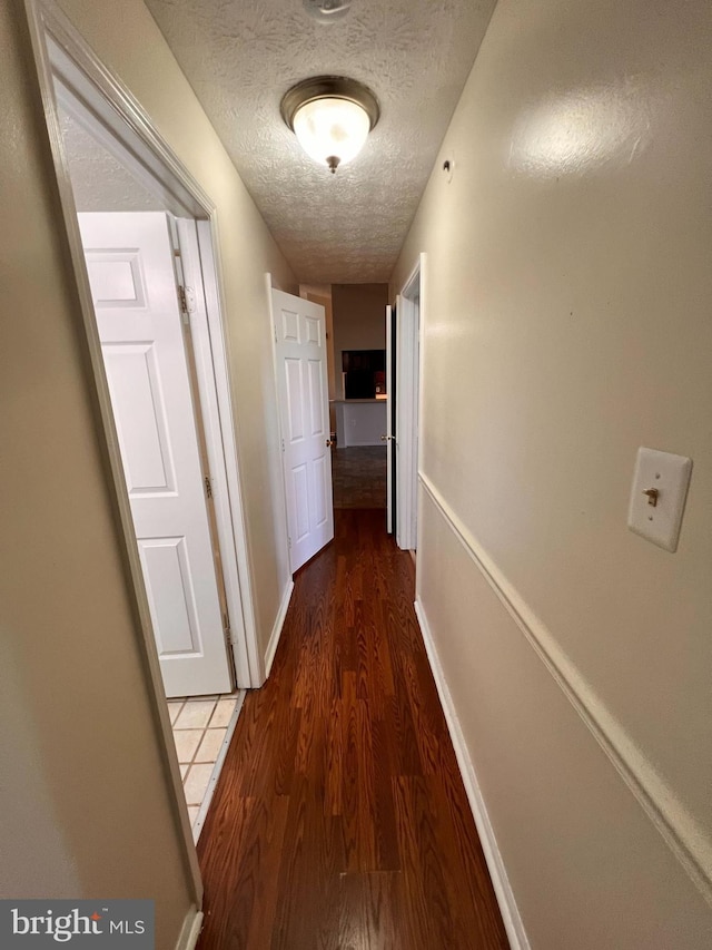 hall with a textured ceiling and dark wood-type flooring