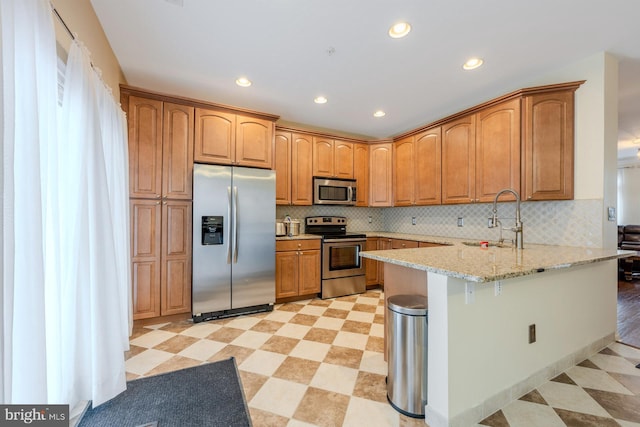 kitchen featuring light stone countertops, sink, kitchen peninsula, a breakfast bar, and appliances with stainless steel finishes