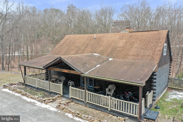 log-style house with a shingled roof, a porch, log siding, and a chimney