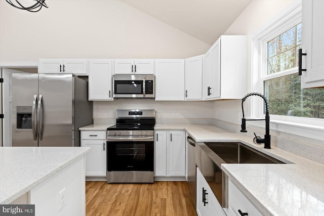 kitchen featuring light stone counters, stainless steel appliances, vaulted ceiling, light hardwood / wood-style floors, and white cabinetry