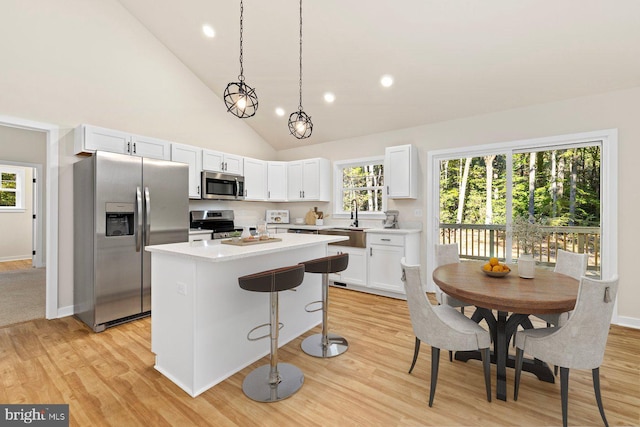 kitchen with stainless steel appliances, a kitchen island, high vaulted ceiling, light hardwood / wood-style floors, and white cabinetry