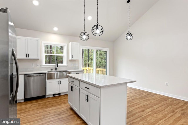 kitchen featuring pendant lighting, lofted ceiling, white cabinets, sink, and appliances with stainless steel finishes