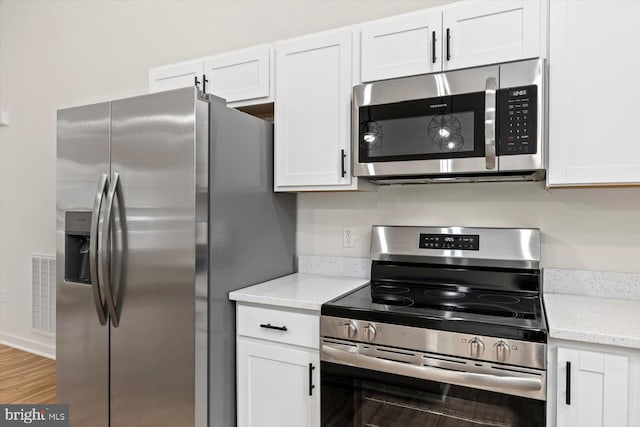 kitchen with white cabinets, light stone countertops, appliances with stainless steel finishes, and light hardwood / wood-style flooring