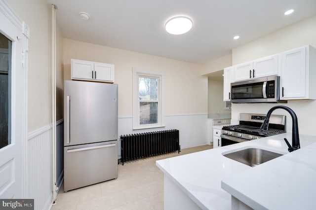 kitchen featuring sink, radiator heating unit, light tile patterned flooring, white cabinetry, and stainless steel appliances