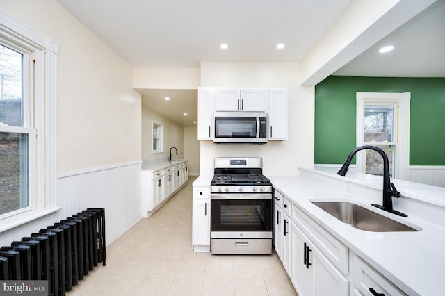 kitchen with appliances with stainless steel finishes, radiator heating unit, white cabinetry, and sink