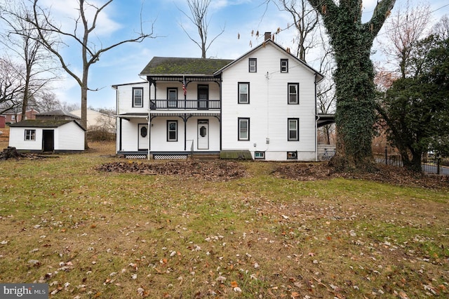 view of property featuring covered porch, a balcony, a shed, and a front yard