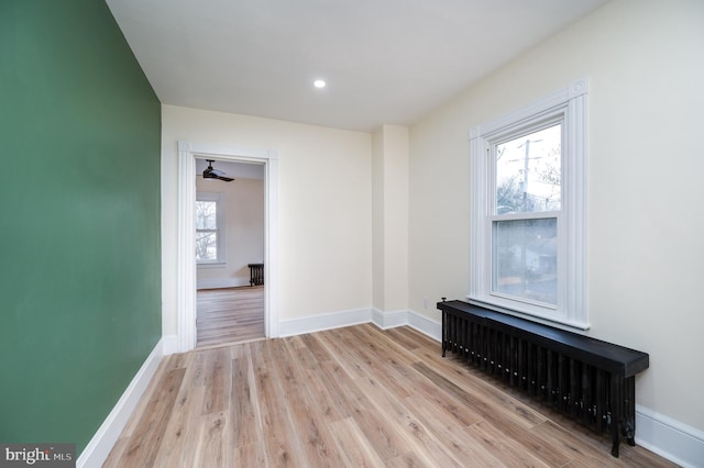 empty room with radiator heating unit, light hardwood / wood-style flooring, a wealth of natural light, and ceiling fan