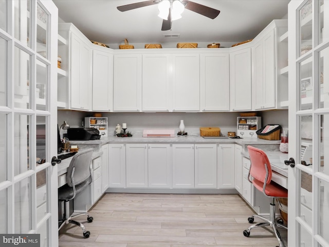 kitchen with white cabinetry, light stone counters, built in desk, and light hardwood / wood-style flooring